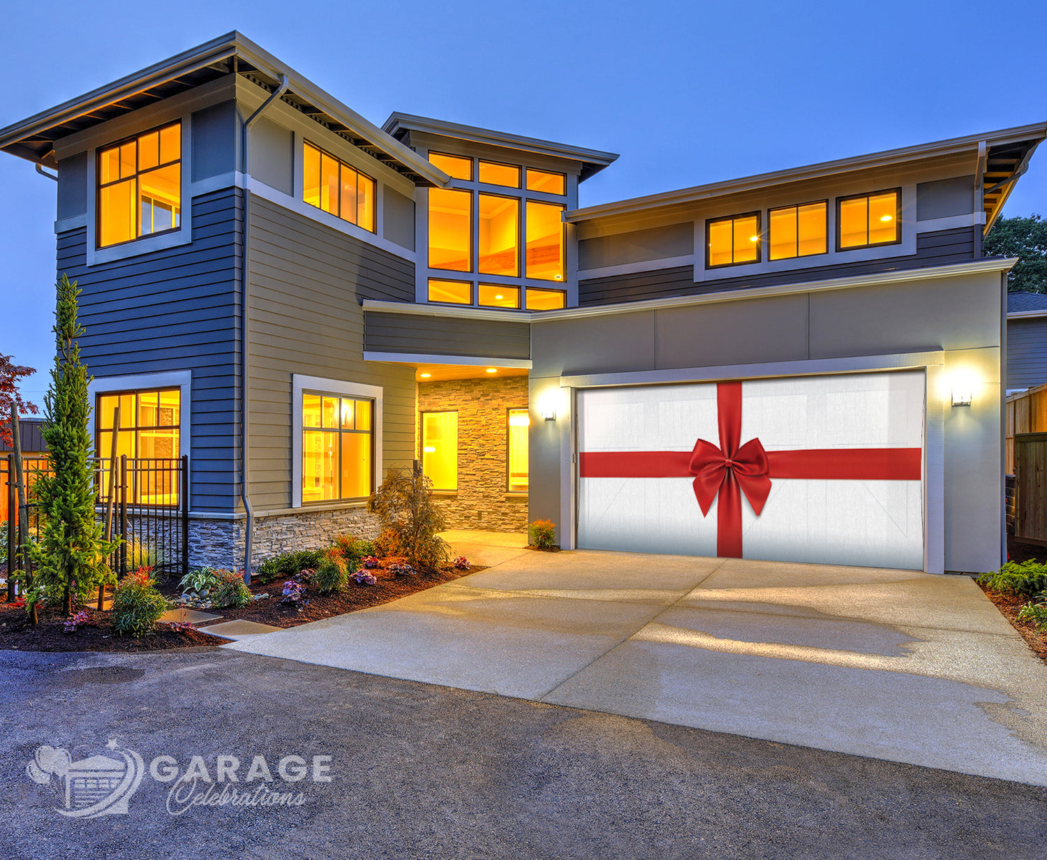Modern house with a decorative garage door featuring a red bow, illuminated windows, and a clear blue sky.